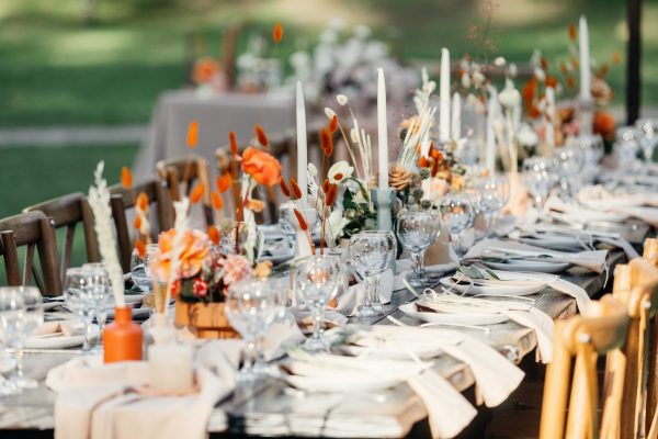 Luxury wedding reception, dining table setup with decoration on rustic wooden table. Dishes, cutlery, napkins and accessories, dry plants, glasses and candles on table for guests, flat lay, outdoor