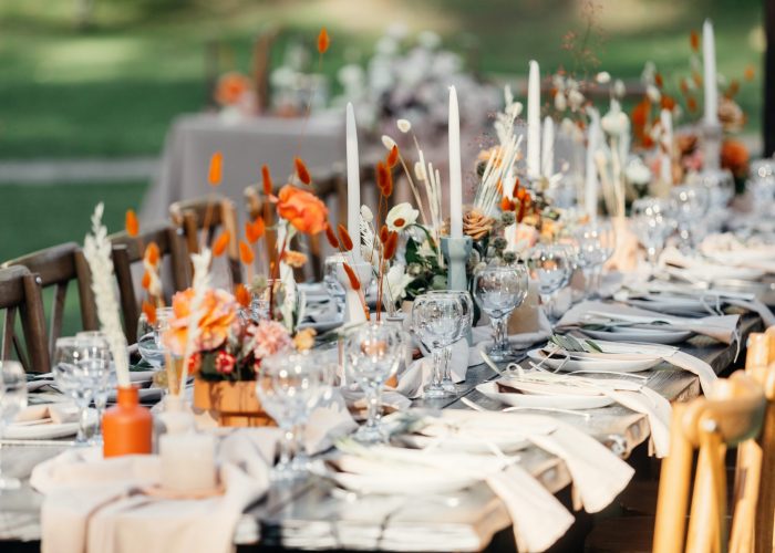 Luxury wedding reception, dining table setup with decoration on rustic wooden table. Dishes, cutlery, napkins and accessories, dry plants, glasses and candles on table for guests, flat lay, outdoor