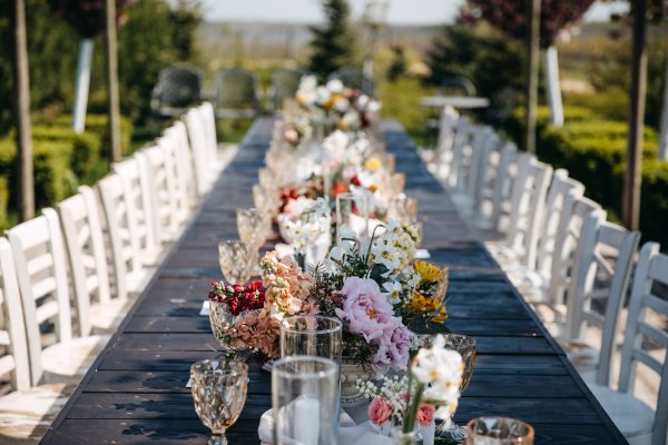 Long wooden table decorated with flowers for an outdoors wedding party.